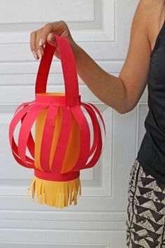 a woman is holding a red and yellow paper lantern with tassels on it