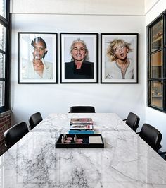 three framed photographs hang on the wall above a marble dining room table with black chairs