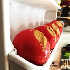 two red apples with gold foil on them sitting in a white container next to an open refrigerator