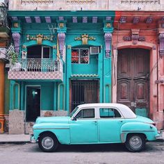 an old blue car parked in front of a building with colorful doors and balconies