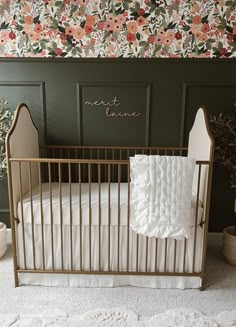 a white crib in front of a wall with flowers on it and a name written on the side