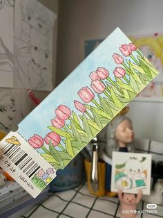 a person holding up a piece of paper with flowers painted on it in the kitchen