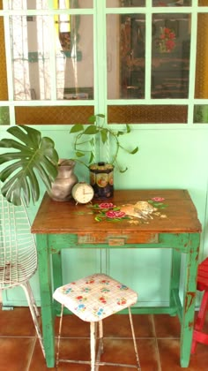 a green table with two chairs and a potted plant on it in front of a window