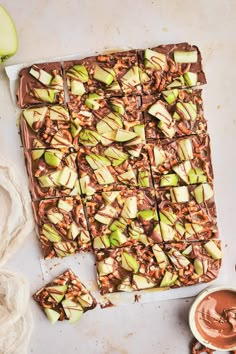 chocolate caramel apple barkle squares on a white surface with apples and cinnamon in the background