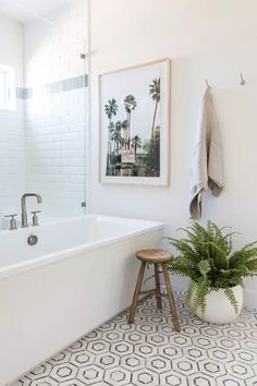 a bathroom with a white bath tub sitting next to a wooden stool and green plant