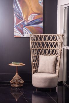 a wicker chair sitting next to a table with a painting on the wall behind it