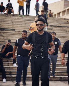 a man in black shirt and suspenders walking down stairs with other people behind him