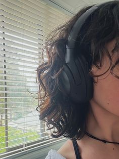 a close up of a person wearing headphones in front of a window with blinds