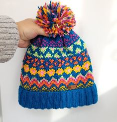 a hand holding a colorful knitted hat with pom - pom on it