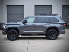 a gray suv parked in front of garage doors with black rims and red tires