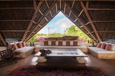 a living area with couches, tables and chairs under a thatched roof over looking the water