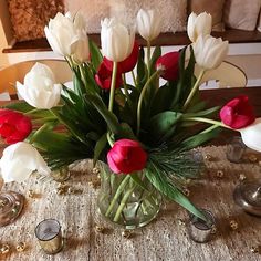 a vase filled with red and white flowers on top of a table next to candles