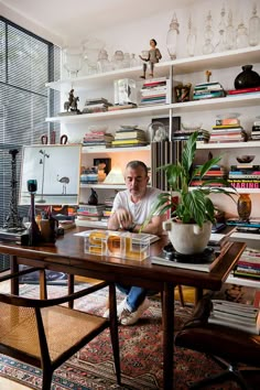 a man sitting at a wooden table in front of a book shelf filled with books