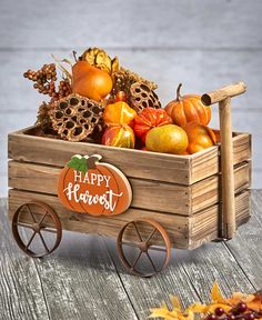 a wooden wagon filled with lots of fruit on top of a wooden table next to pumpkins