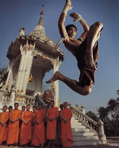 a group of men standing around each other in front of a building with a man jumping up into the air