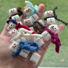 a hand holding several small snowmen made out of plastic cubes and string wrapped around them