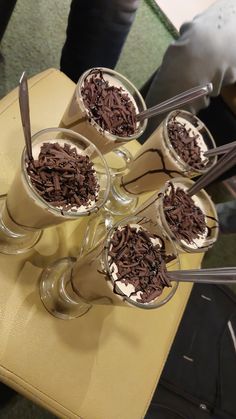 four glasses filled with ice cream and chocolate shaving on top of a yellow table