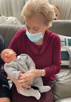 an older woman holding a baby wearing a face mask