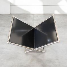 an upside down black and silver object on concrete floor with white wall in the background