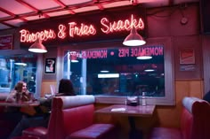 two people sitting at a table in front of a restaurant with neon signs above them