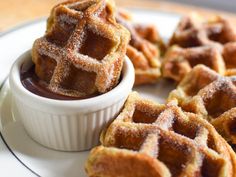 some sugared waffles are in a small bowl on a plate with chocolate sauce