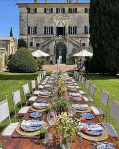 a long table set with plates and place settings in front of an old building on a lawn