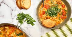 two pans filled with soup and bread on a marble counter top next to each other