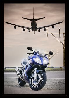 a blue motorcycle is parked in front of an airplane that is flying over the ground