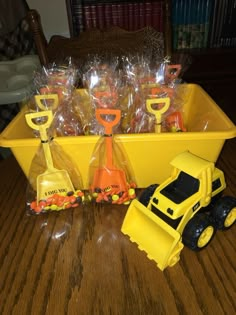 a yellow toy truck filled with plastic bags and orange construction equipment on top of a wooden table