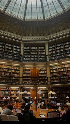 people sitting at tables in a library with many bookshelves and glass ceiling lights