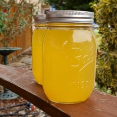 two jars filled with yellow liquid sitting on top of a wooden table