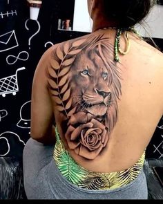 a woman with a lion and rose tattoo on her back shoulder, sitting in front of a wall