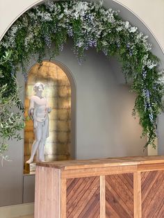 a statue in the middle of a room with flowers and greenery on the wall