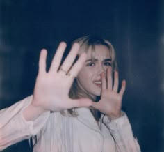 a woman with her hand up in the air while wearing a white shirt and gold bracelet