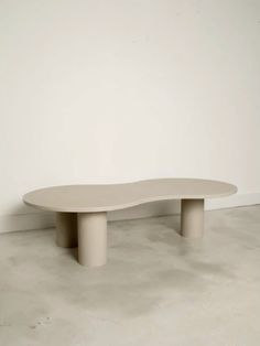 an oval shaped table sitting on top of a cement floor next to a white wall