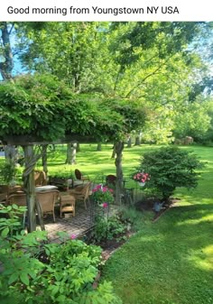 an outdoor dining area in the middle of a yard with trees and flowers around it