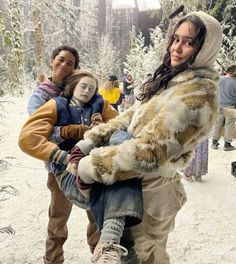 a woman carrying a child in the snow with other people around her and trees behind her