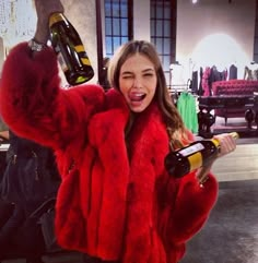 a woman in a red fur coat holding two wine bottles