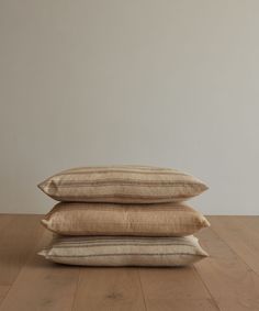 three pillows stacked on top of each other in front of a white wall and wooden floor