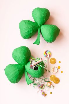 two green paper shamrocks next to some candies on a white surface with gold coins