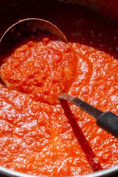 a ladle full of tomato sauce being stirred with a wooden spoon in the pot