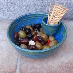 a blue bowl filled with assorted olives and anchovies next to a wooden stick