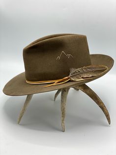 Dress weight beaver felt in color Pecan Teardrop crown, 3 3/4" tall Snap, flanged brim, 3" wide Elk leather tie and feather Hand-stitched mountain detail This felt hat is made to order, please allow 6-8 weeks for delivery. Nick Fouquet Hats, Custom Cowboy Hats, Custom Made Hats, Mountain Logo, Mens Hats Fashion, Antler Art, Classy Outfits Men, Felt Cowboy Hats, Felt Hats