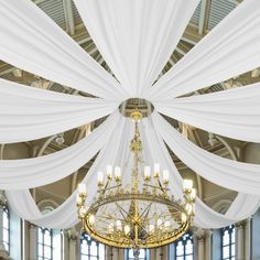 a chandelier hanging from the ceiling in a large room with white drapes