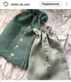 two green bags with flowers on them sitting on top of a white tablecloth next to each other