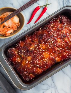 a pan filled with meat and vegetables next to chopsticks on a marble counter top