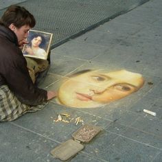 a man sitting on the ground drawing with his face in chalk next to a sidewalk