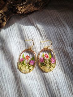 a pair of earrings with flowers in them on a white cloth background and a piece of wood