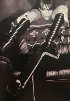 black and white photograph of young man sitting on leather chair with his legs crossed in the air