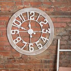 a white clock mounted to the side of a red brick wall next to a chair